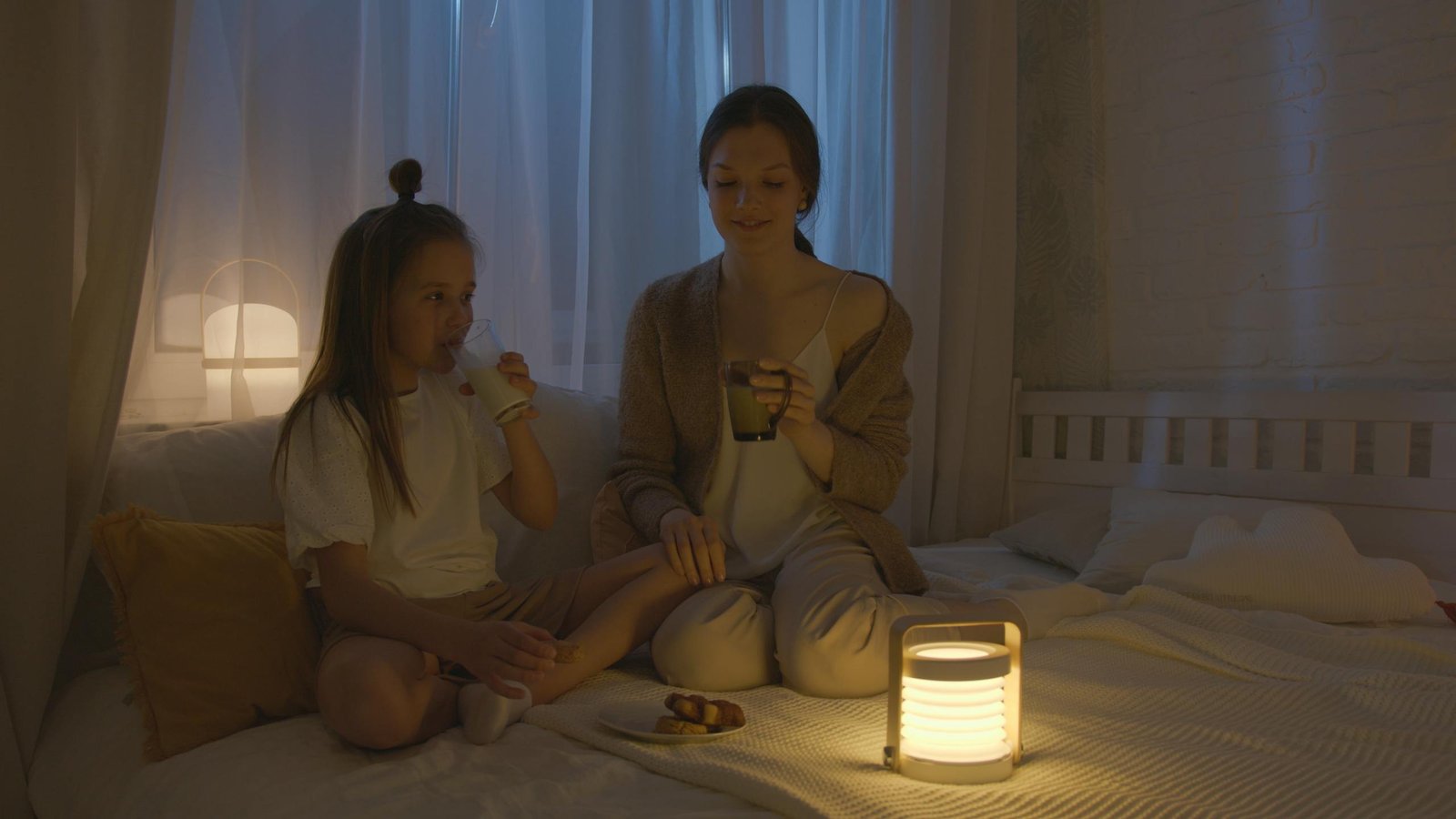 A mother and daughter bonding over milk and snacks in a cozy bedroom setting.