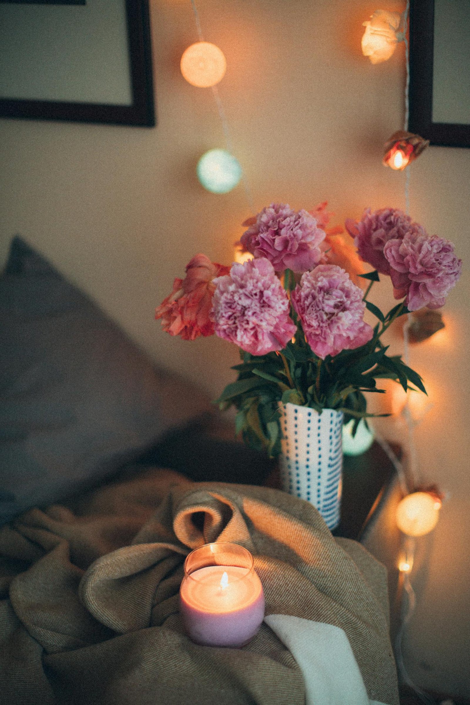 Inviting cozy bedroom corner with peony flowers, candle, and ambient lighting creating a warm atmosphere.