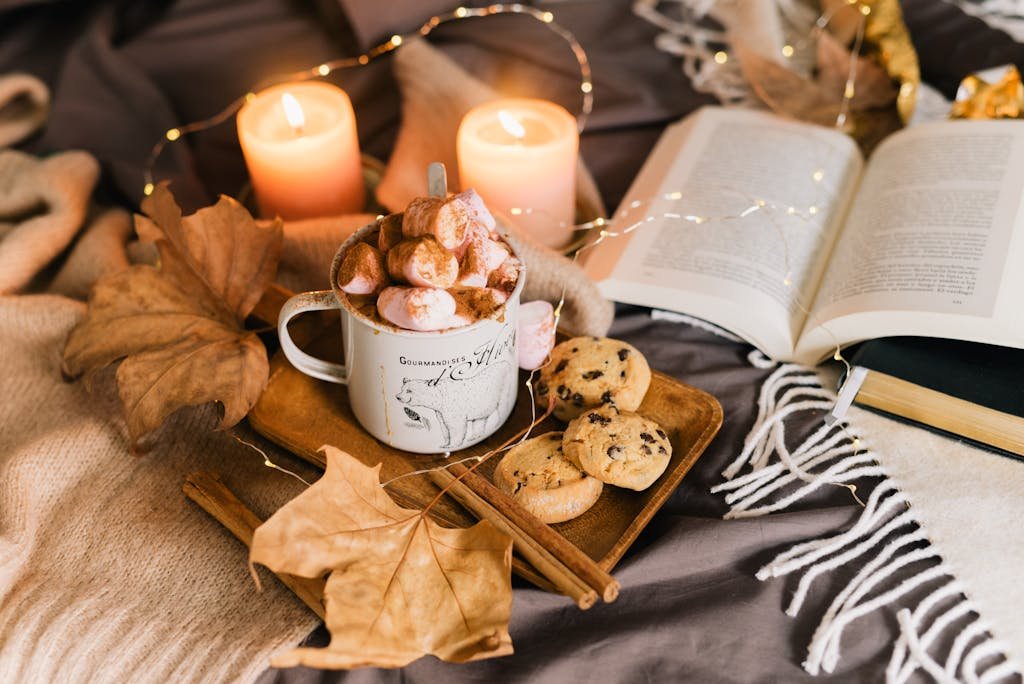 Warm autumn setup with hot chocolate, cookies, book, and candles.